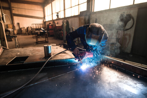 Professional welder welding metal construction parts industrial workshop